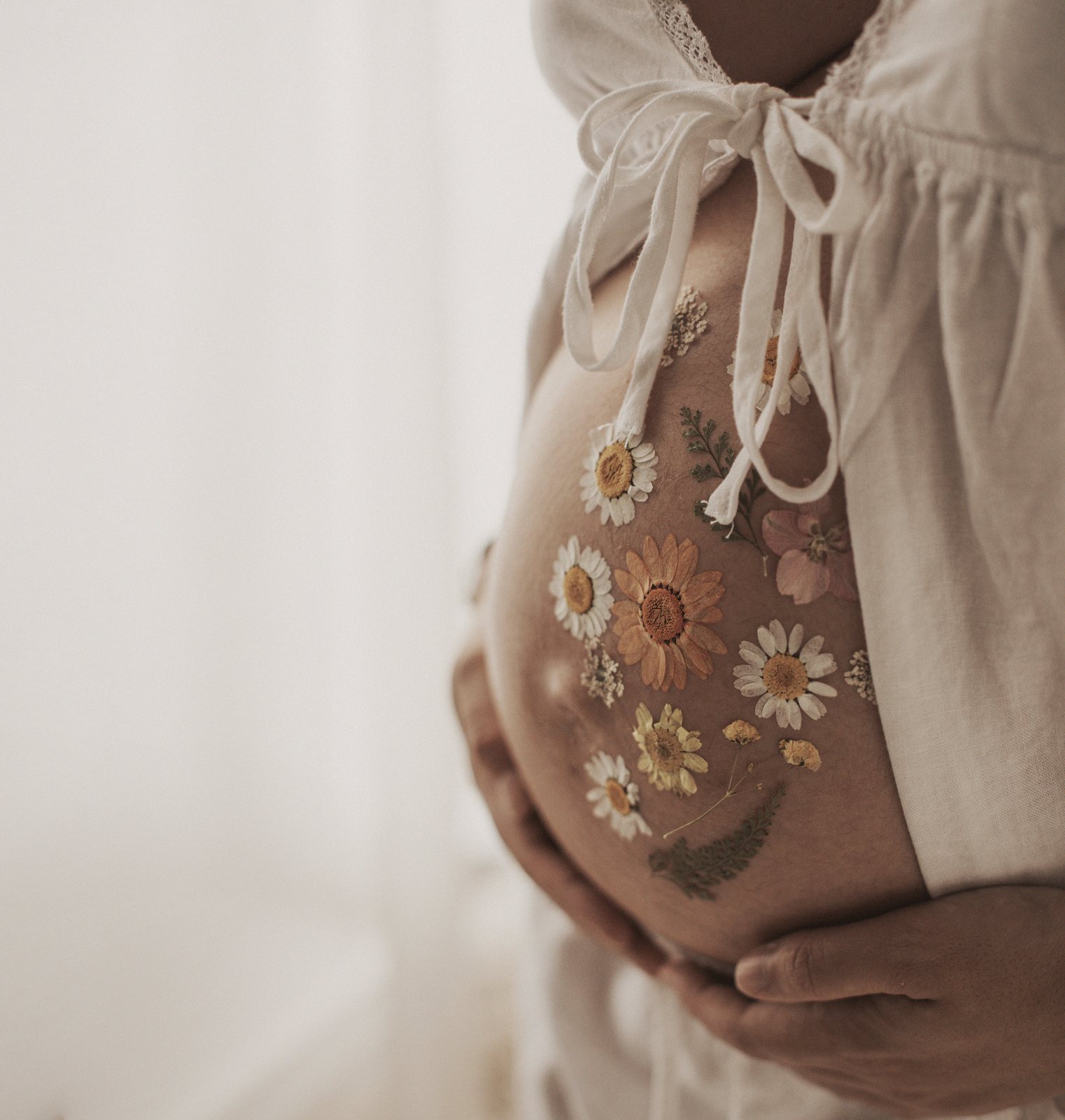 Detalle de la barriga de una embarazada con vestido de flores en una fotografía fine art