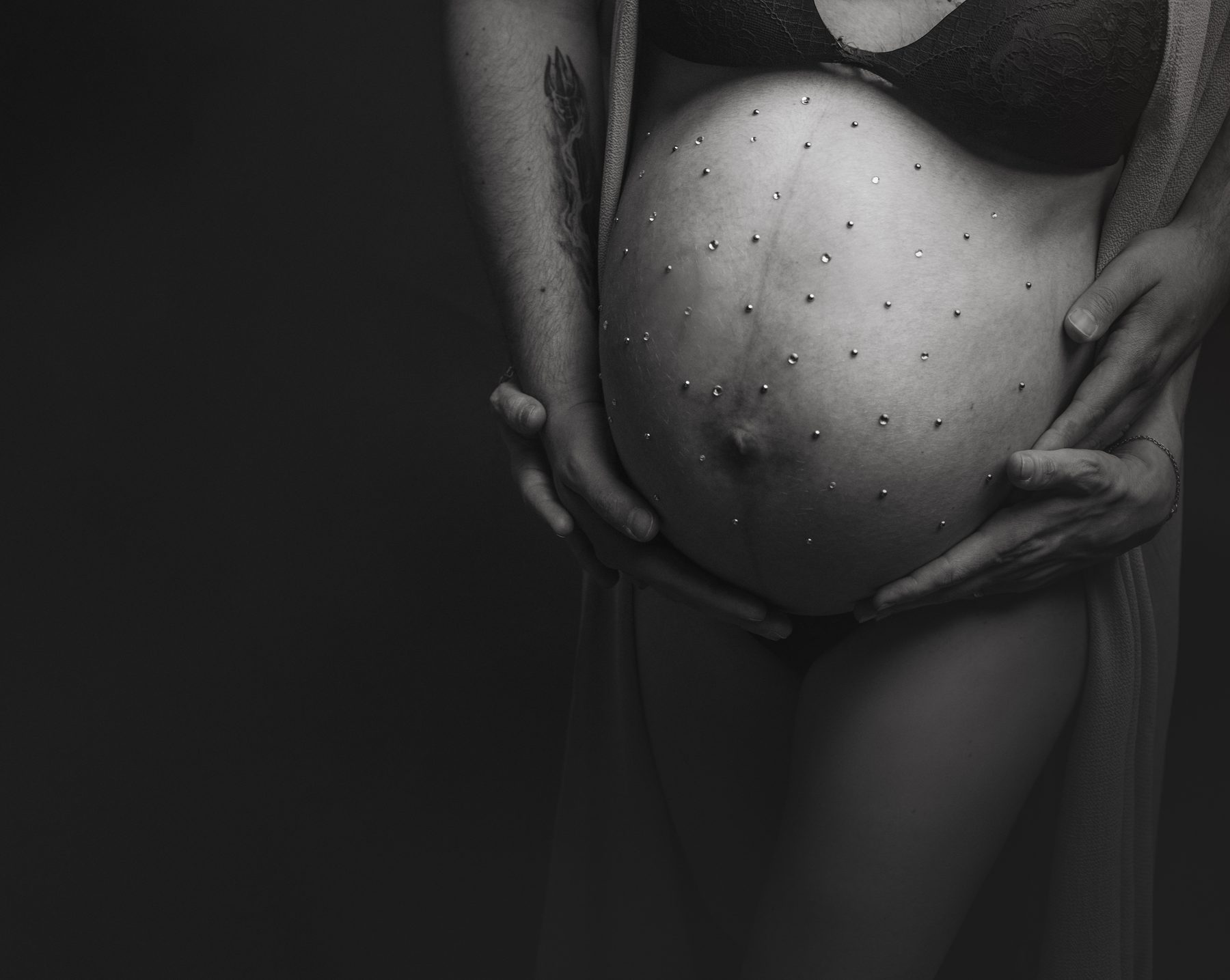 Detalle en blanco y negro de las manos sobre la barriga en una sesión de embarazo