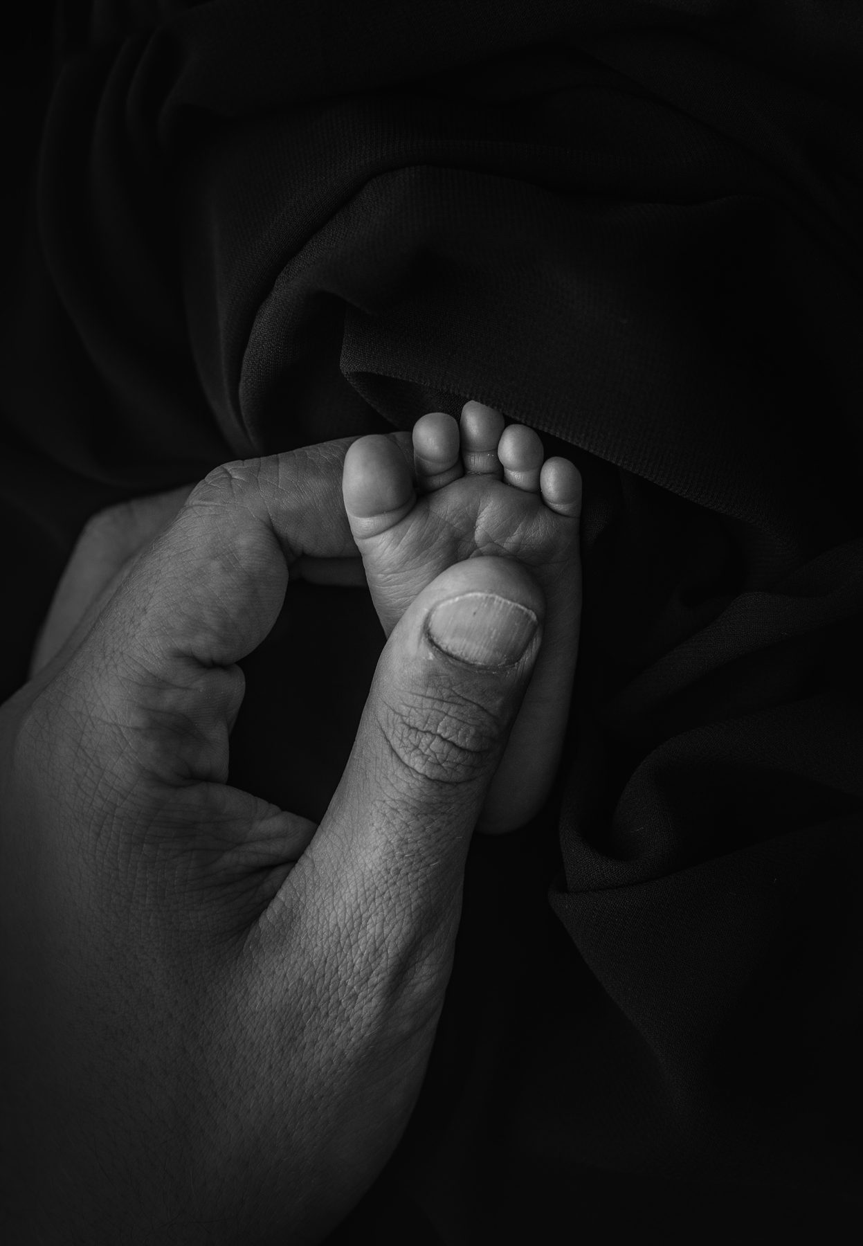 Detalle en blanco y negro de los pies de un recién nacido sobre la mano de su padre