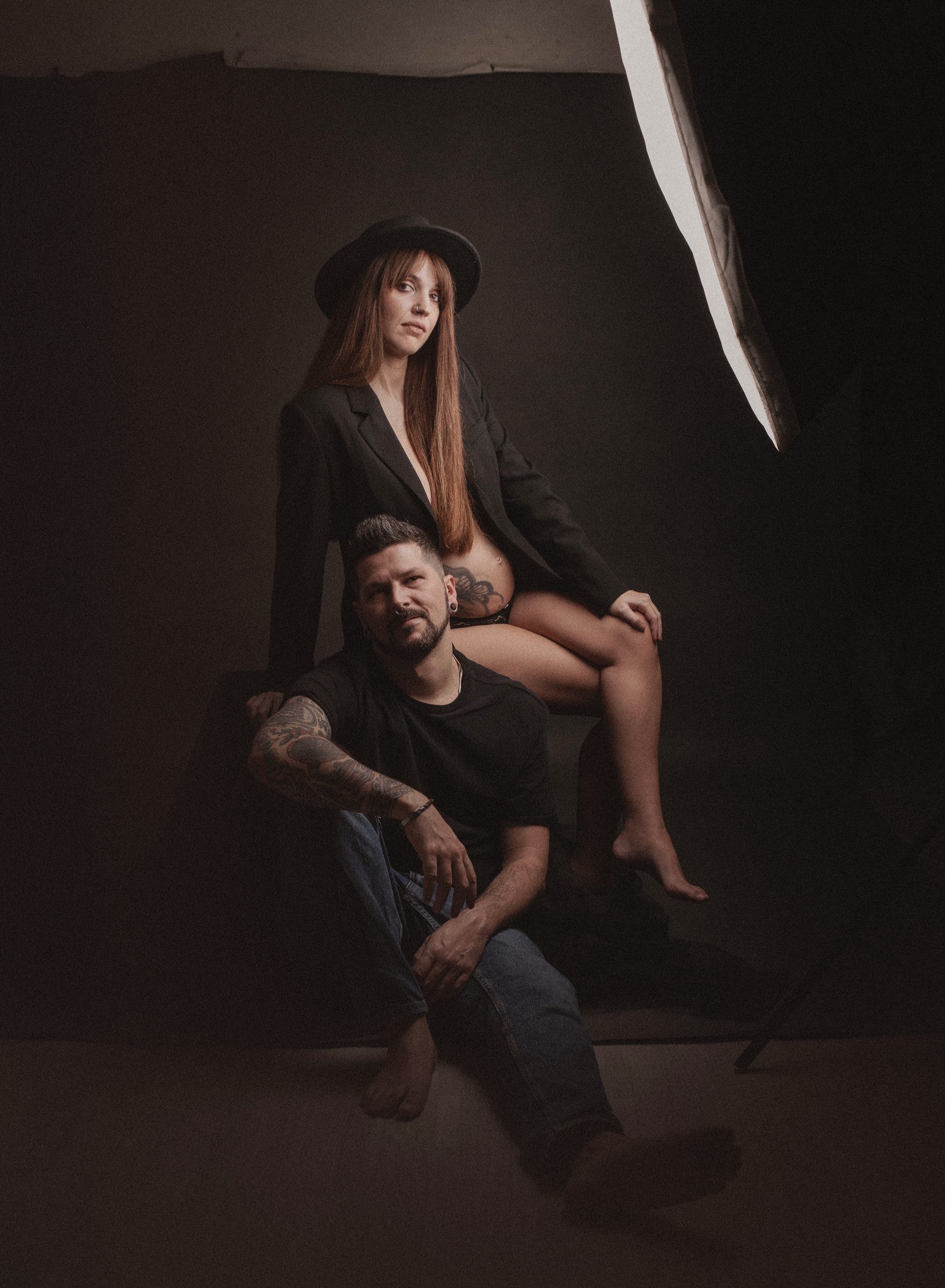 Pareja en el estudio, ella embarazada con sombrero sentada sobre él