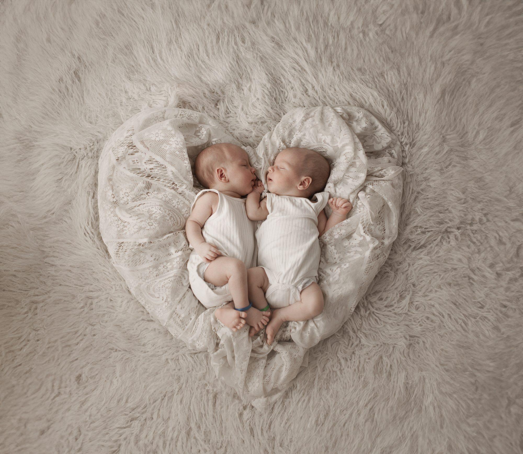 Gemelos recién nacidos dormidos dentro de un corazón de tela clara
